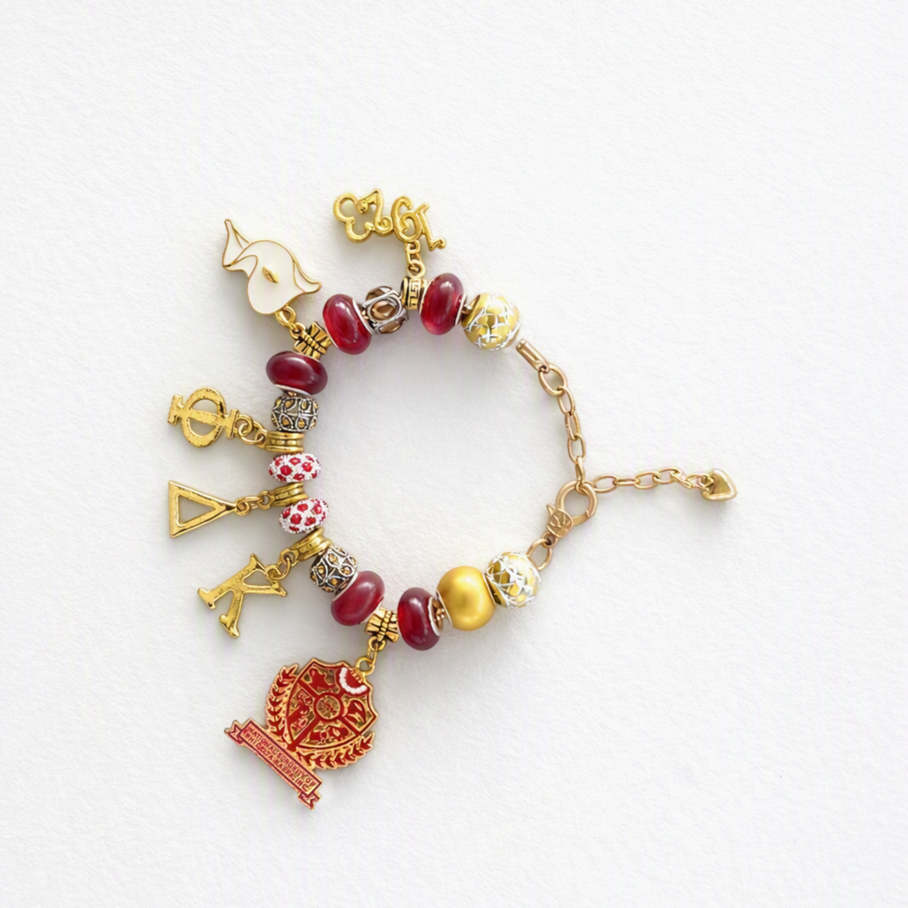 Pat Goffe Collections gold-tone charm bracelet featuring red and patterned beads with Greek letter and crest charms.