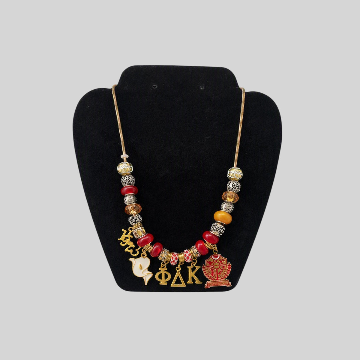 Pat Goffe Collections charm necklace featuring red and gold beads with Greek letter and crest charms on a gold chain