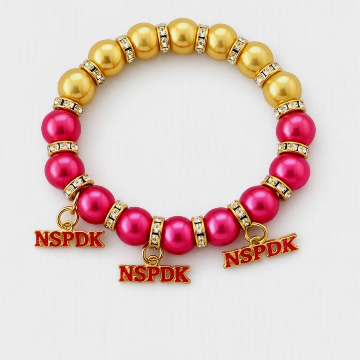 Pat Goffe Collections NSPDK stretch bracelet featuring pink and gold beads with crystal spacers and three charms.