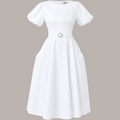 Pat Goffe Collections white midi dress featuring puff sleeves, a belted waist, and an embroidered NSPDK crest.