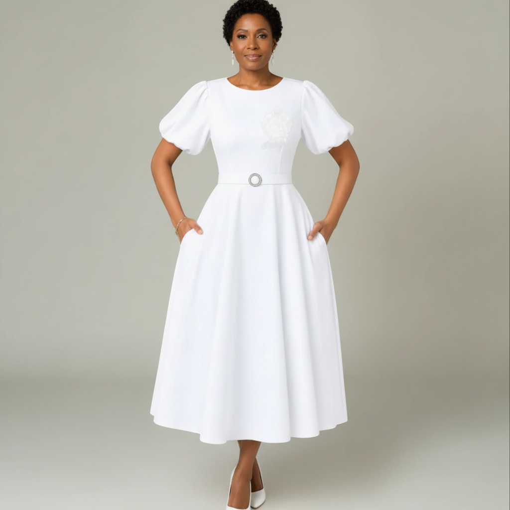 Pat Goffe Collections white midi dress with puff sleeves, belted waist, and embroidered crest on a model